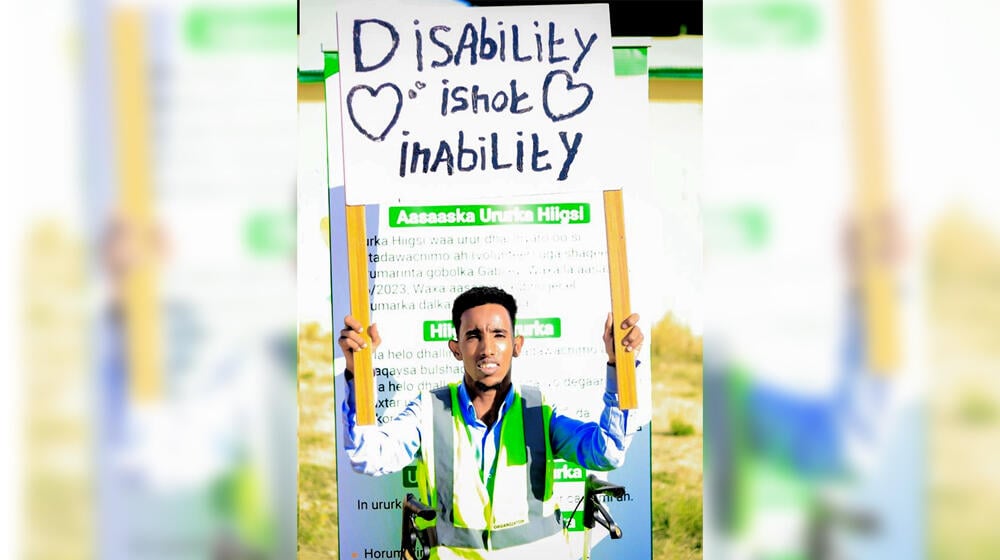 Mustafa Mohamed holds up a sign that reads 'Disability is not Inability'